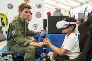A child wearing a virtual reality headset with googles and a pilot in front of him in the Techno Zone at RIAT24.
